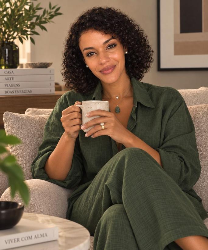 Carmen Amaral sentada no sofá, a sorrir, com uma caneca nas mãos